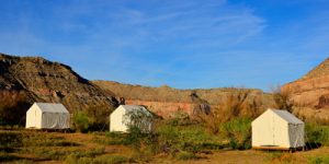 four tents sit on platforms in the hilly desert under a clear blue sky"