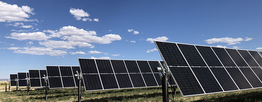 An array of solar panels against a blue sky dotted with white clouds.