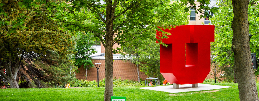 A huge sculpture of a red block U on the University of Utah campus among green trees and lawn.